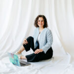 „Belinda, Gründerin von BÉLIE Weddings, sitzt entspannt auf dem Boden in legerer Pose neben ihrem Laptop, lächelt in die Kamera und vermittelt ihre lockere, strukturierte Herangehensweise an individuelle Hochzeitsplanung in Wien und Österreich.“