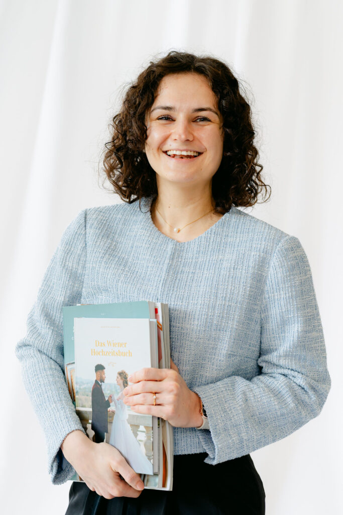 Hochzeitsplanerin Belinda steht lächelnd mit dem Wiener Hochzeitsbuch in den Händen – individuelle Hochzeitsplanung in Wien, Österreich und für Destination Weddings